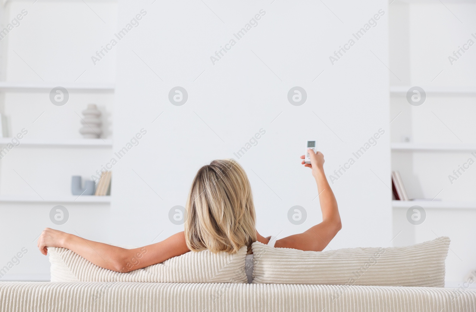 Woman using remote to control air conditioner on sofa at home, back view Photo of Woman using remote to control air conditioner on sofa at home, back view