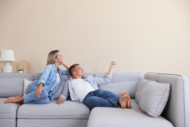 Photo of Woman and man using remote to control air conditioner on sofa at home