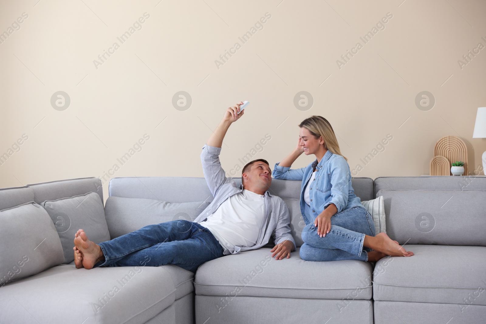 Woman and man using remote to control air conditioner on sofa at home Photo of Woman and man using remote to control air conditioner on sofa at home