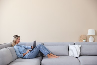 Photo of Beautiful woman using laptop on sofa at home. Space for text