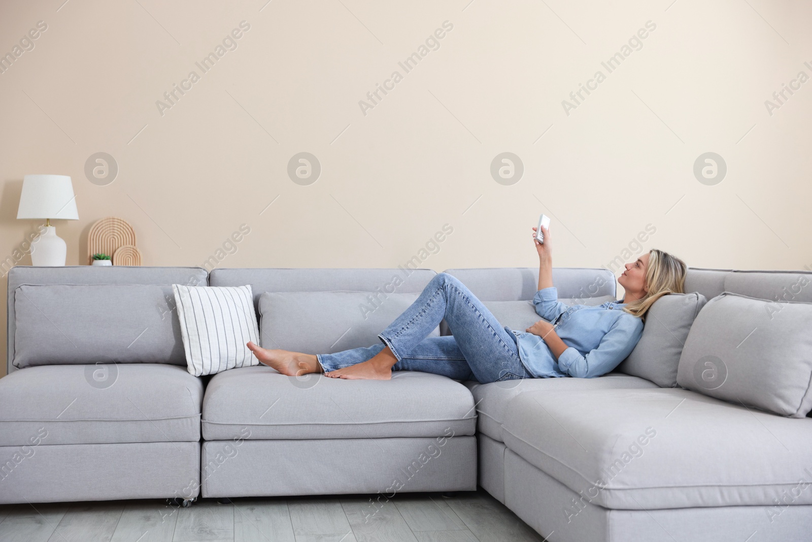 Woman using remote to control air conditioner on sofa at home Photo of Woman using remote to control air conditioner on sofa at home