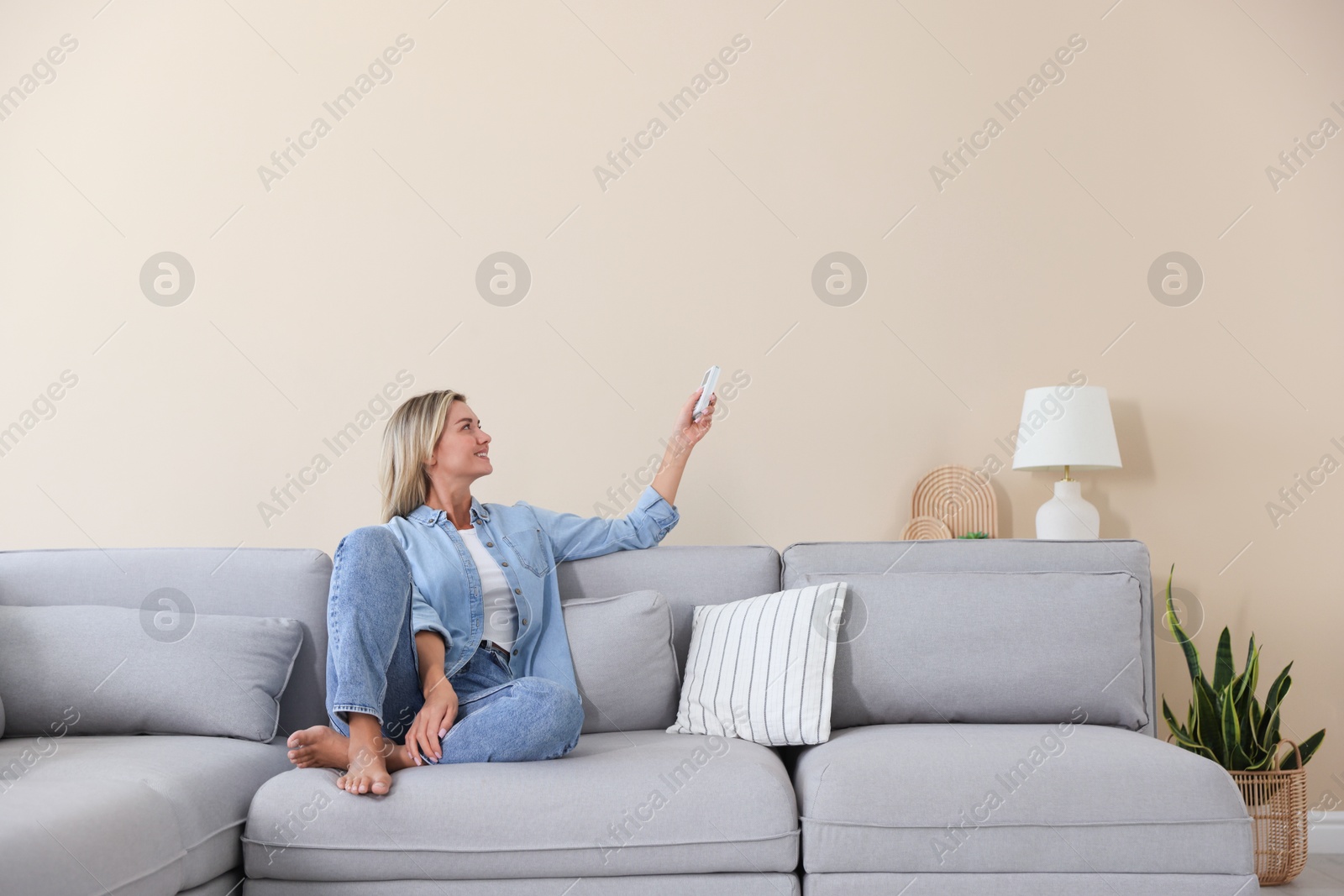Woman using remote to control air conditioner on sofa at home Photo of Woman using remote to control air conditioner on sofa at home