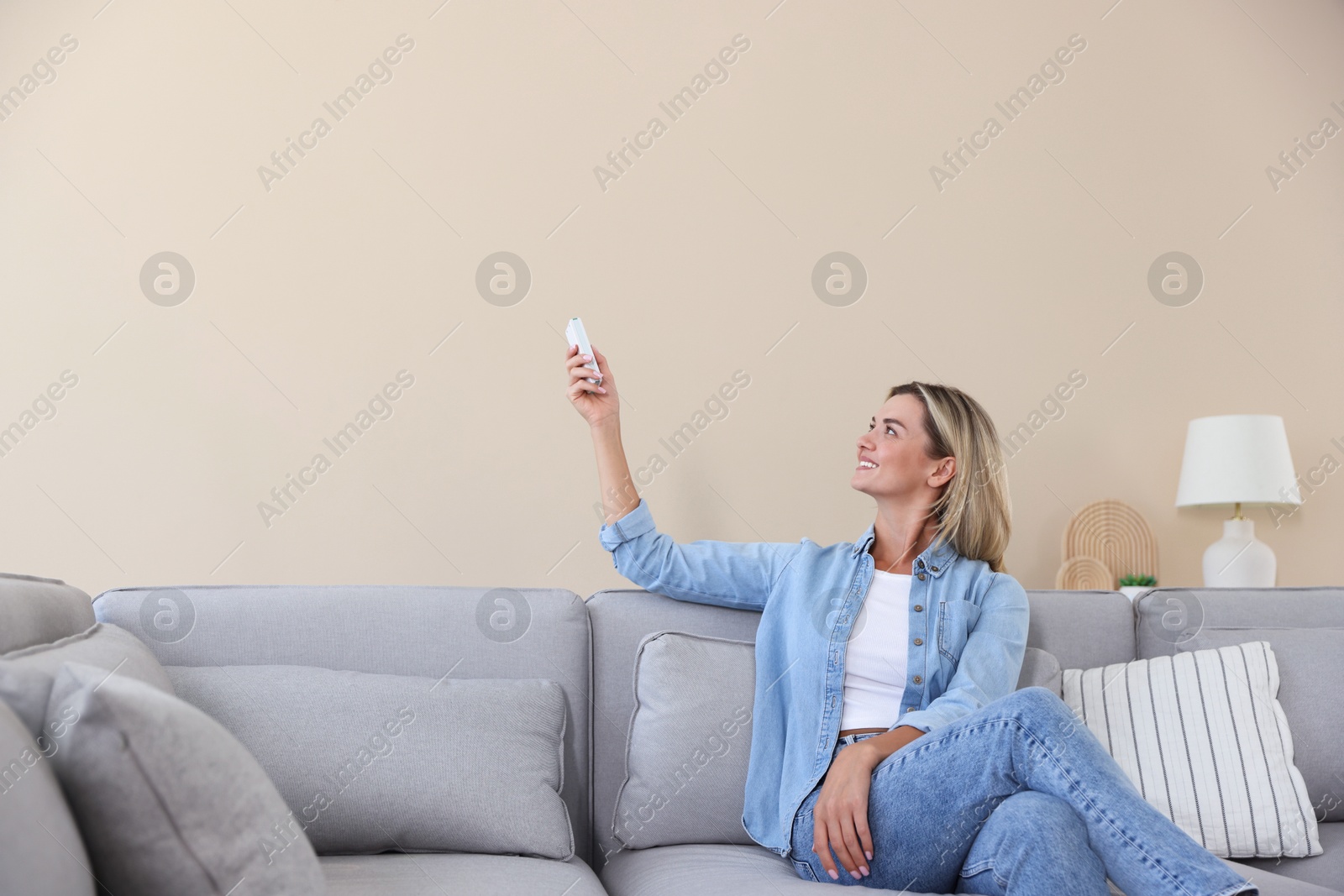 Woman using remote to control air conditioner on sofa at home Photo of Woman using remote to control air conditioner on sofa at home