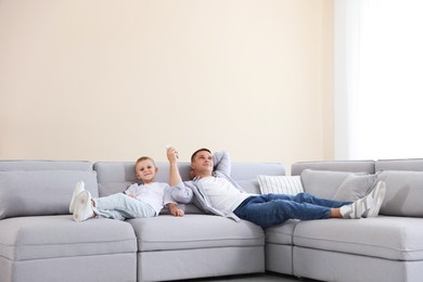 Photo of Little boy and his father using remote to control air conditioner on sofa at home
