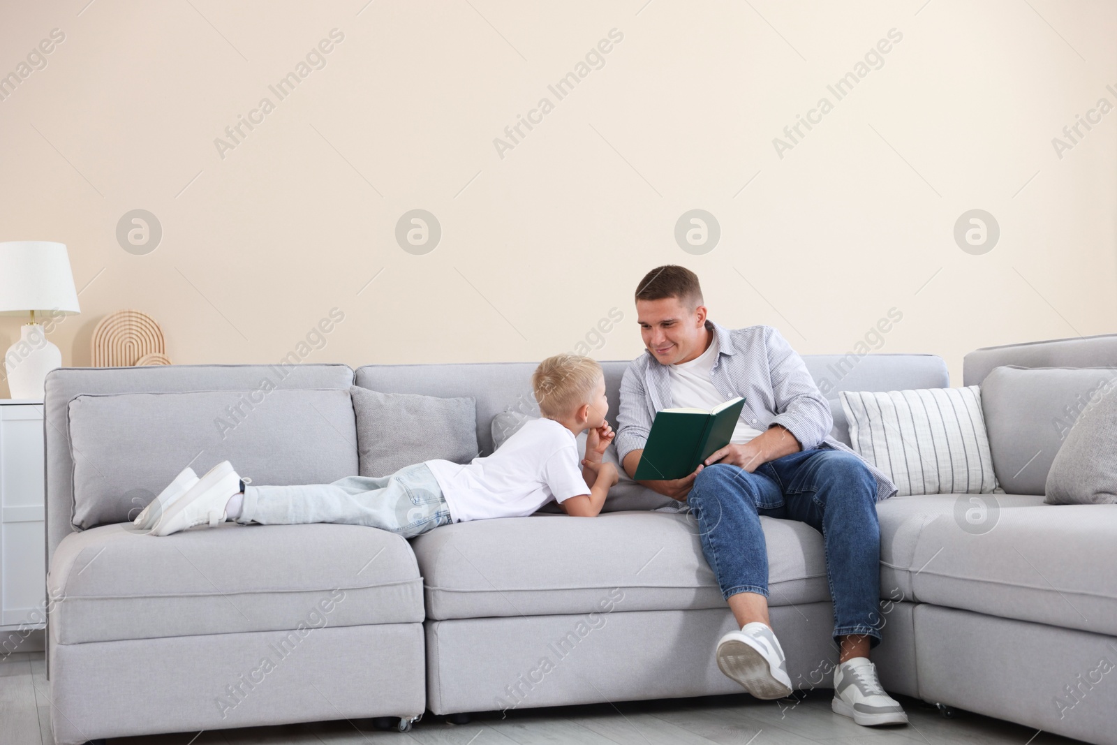Father and his son reading book on sofa at home Photo of Father and his son reading book on sofa at home