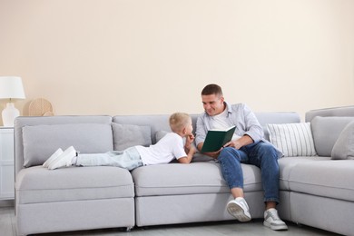 Photo of Father and his son reading book on sofa at home