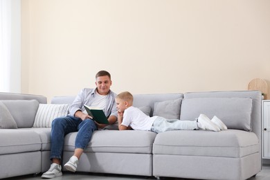Photo of Father and his son reading book on sofa at home