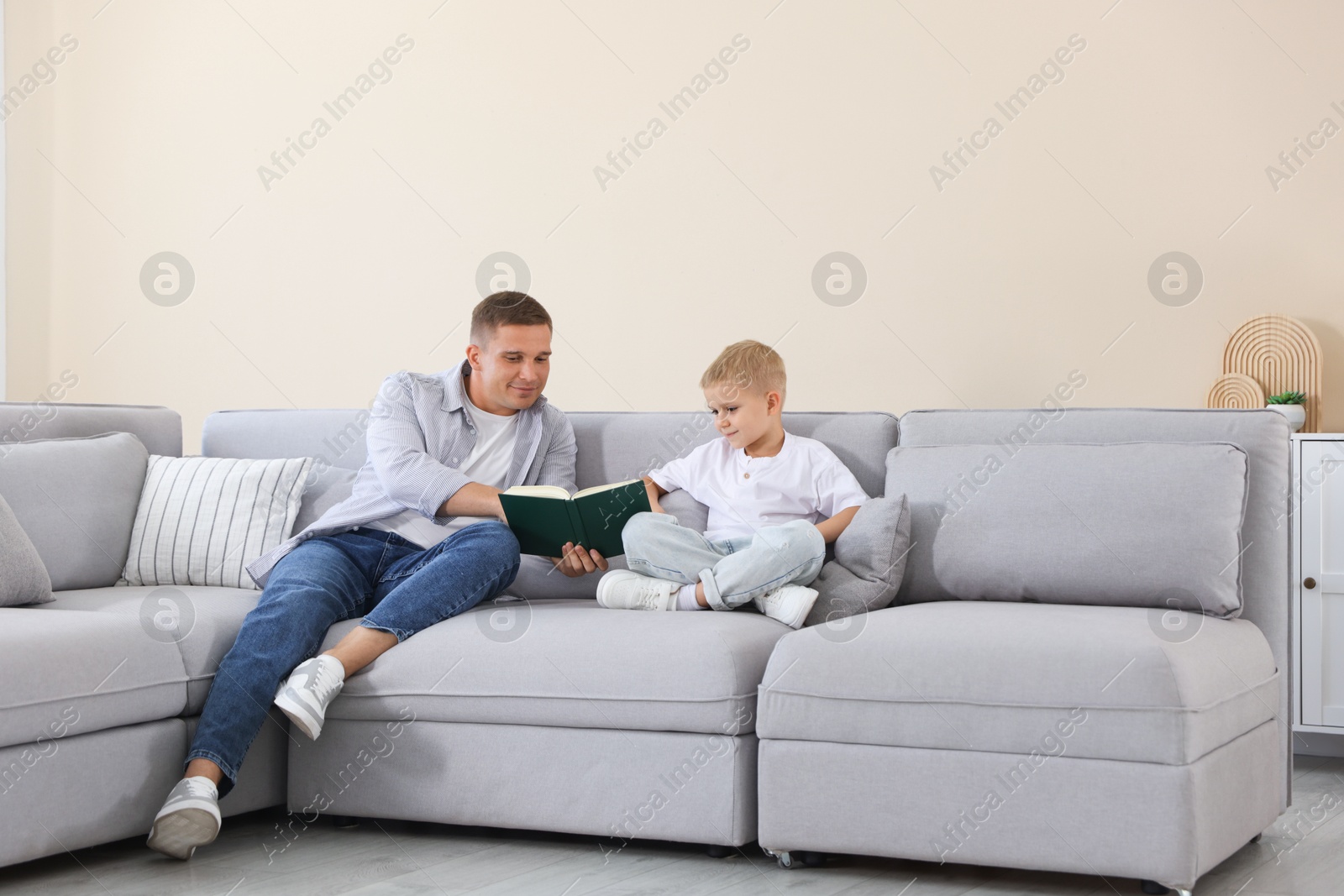 Father and his son reading book on sofa at home Photo of Father and his son reading book on sofa at home
