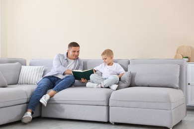 Photo of Father and his son reading book on sofa at home