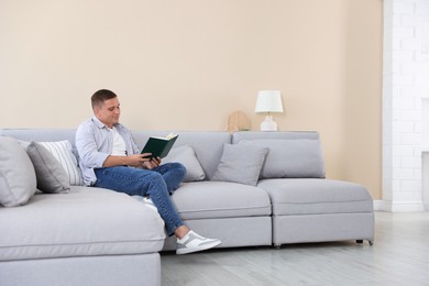 Photo of Young man reading book on sofa at home
