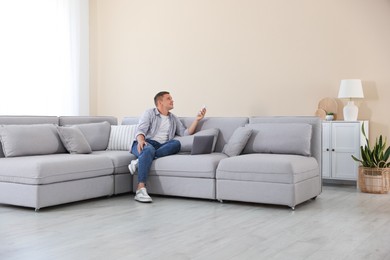 Photo of Man using remote to control air conditioner on sofa at home