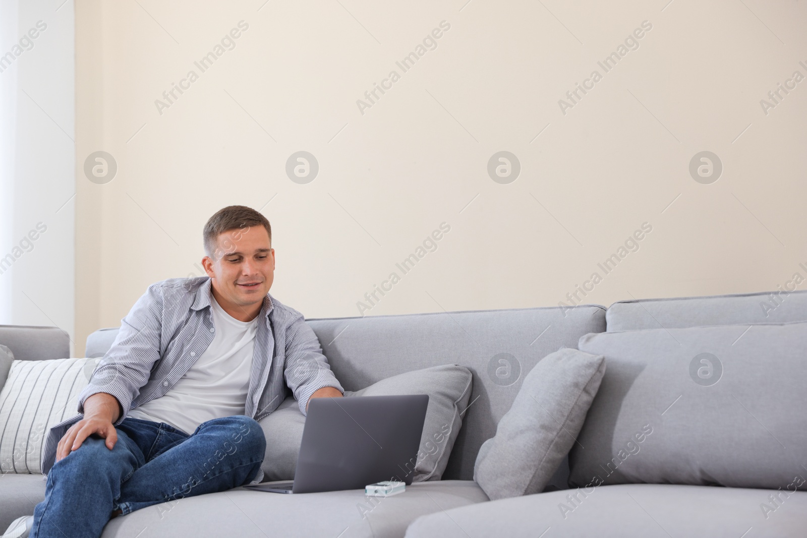 Young man using laptop on sofa at home. Space for text Photo of Young man using laptop on sofa at home. Space for text