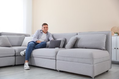 Photo of Young man using laptop on sofa at home