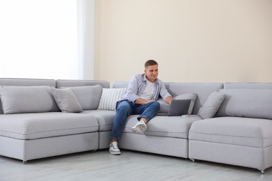 Photo of Young man using laptop on sofa at home