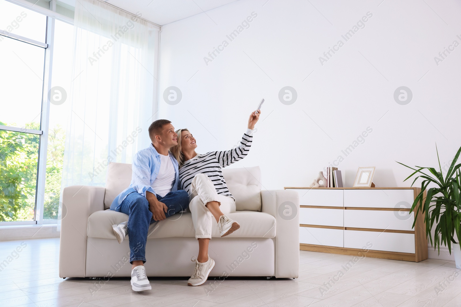 Man and woman using remote to control air conditioner on sofa at home Photo of Man and woman using remote to control air conditioner on sofa at home