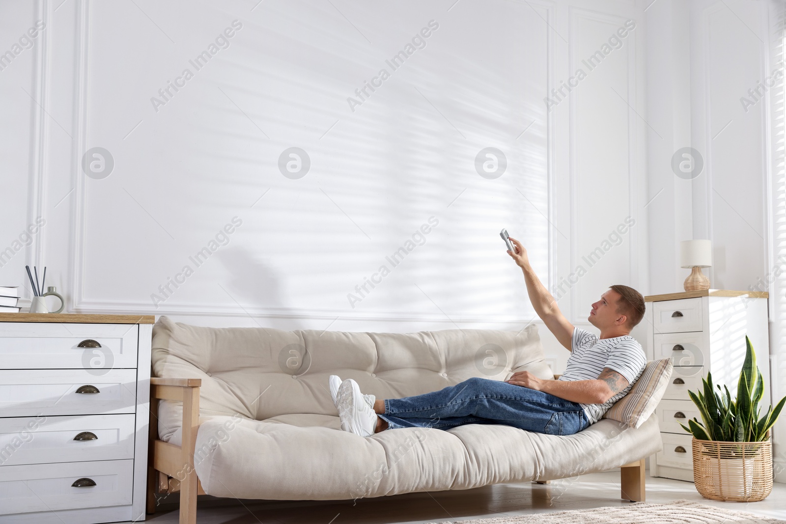 Man using remote to control air conditioner on sofa at home Photo of Man using remote to control air conditioner on sofa at home