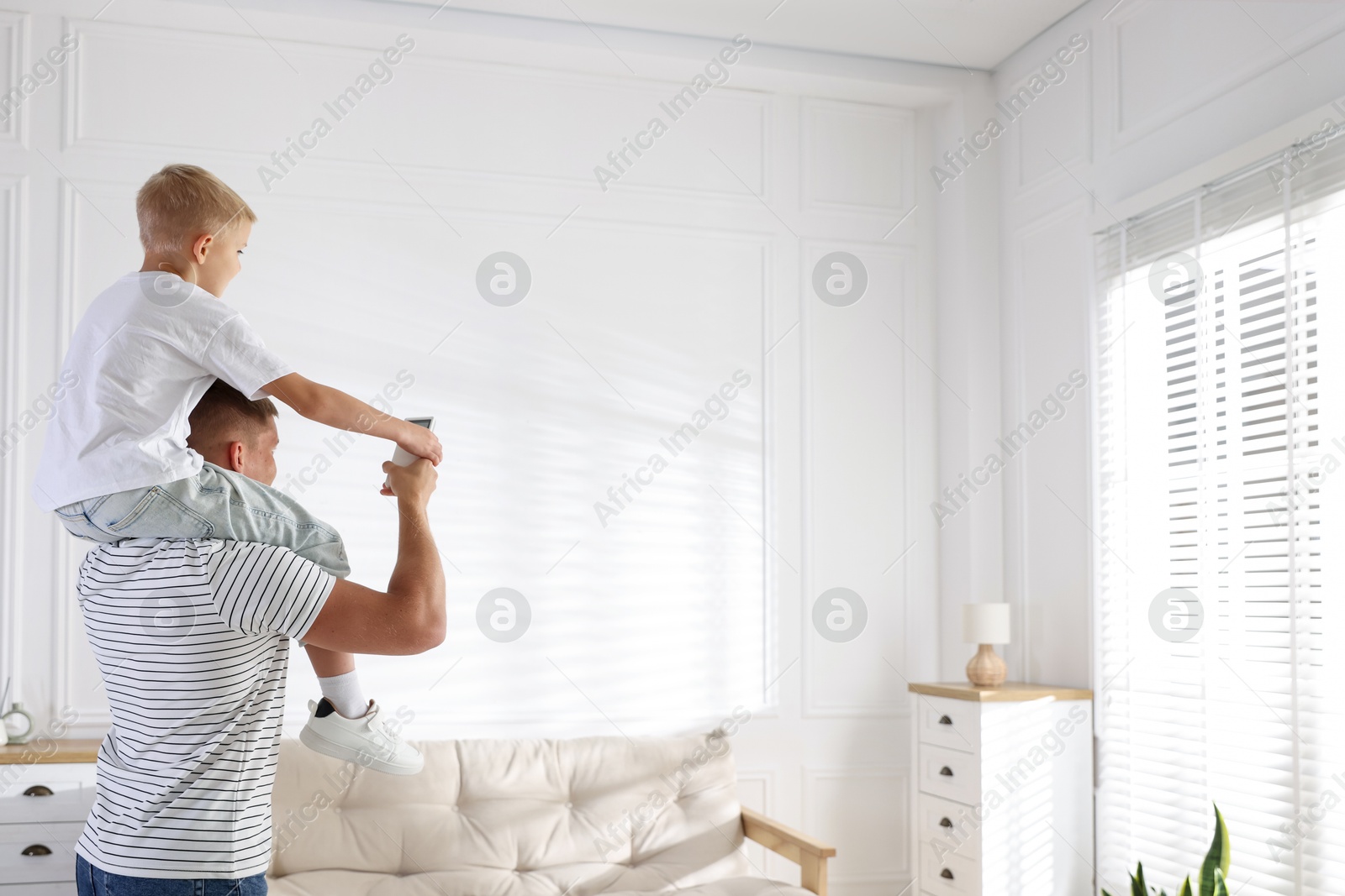 Little boy and his father using remote to control air conditioner at home. Space for text Photo of Little boy and his father using remote to control air conditioner at home. Space for text