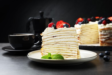 Photo of Piece of tasty crepe cake with berries served on grey table, closeup