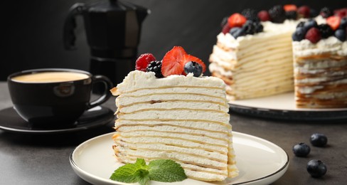 Photo of Piece of tasty crepe cake with berries served on grey table, closeup