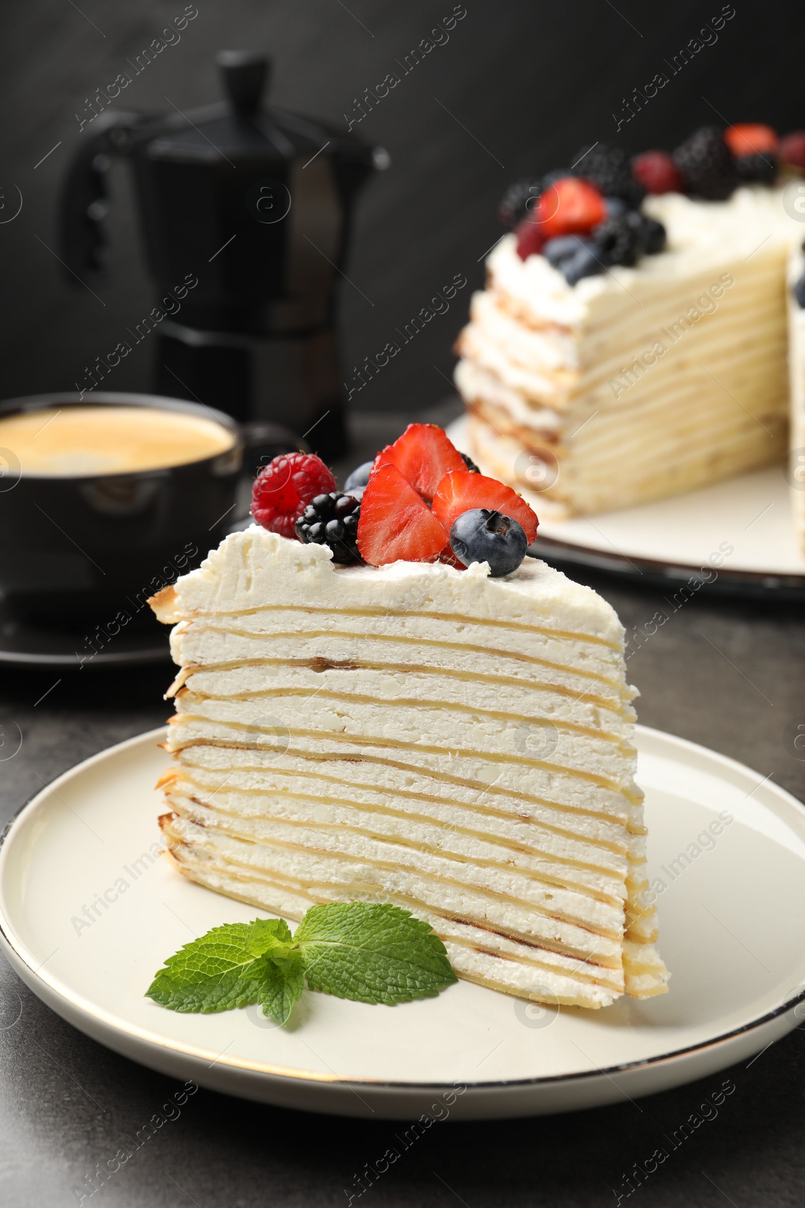 Photo of Piece of tasty crepe cake with berries served on grey table, closeup