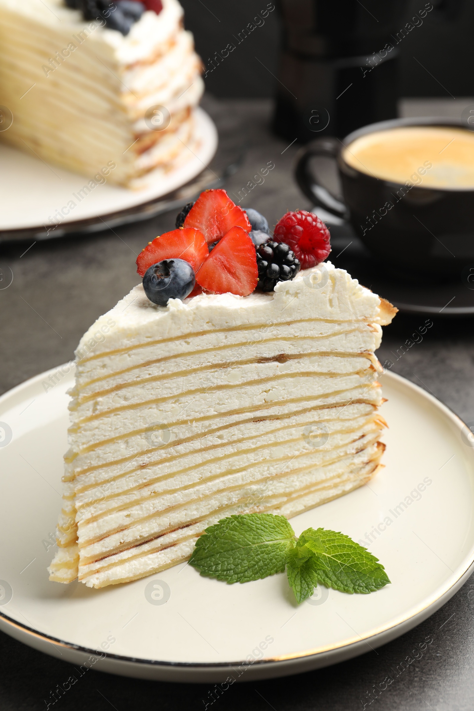 Photo of Piece of tasty crepe cake with berries served on grey table, closeup