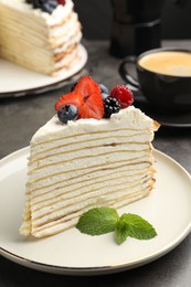Photo of Piece of tasty crepe cake with berries served on grey table, closeup