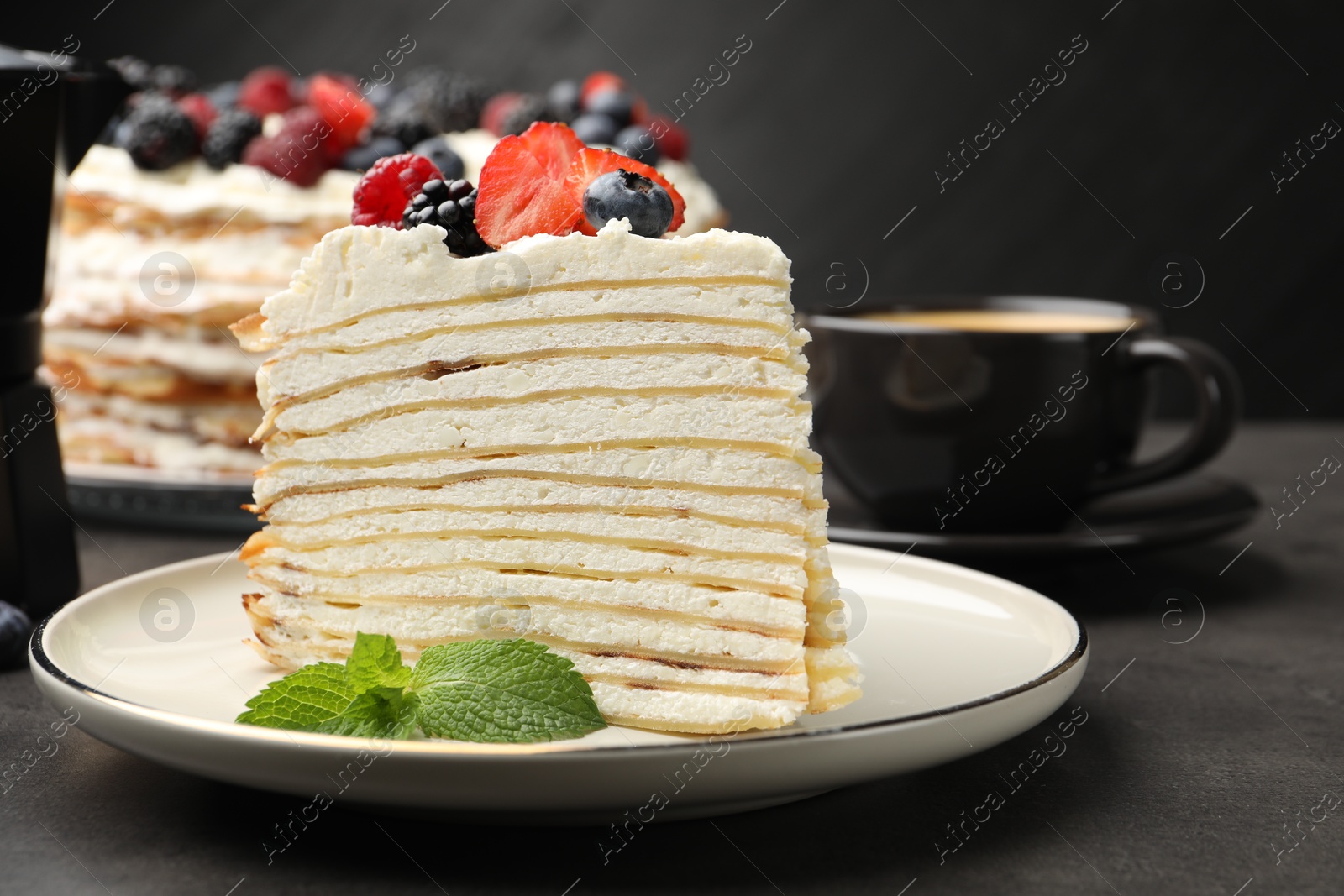 Photo of Piece of tasty crepe cake with berries served on grey table, closeup