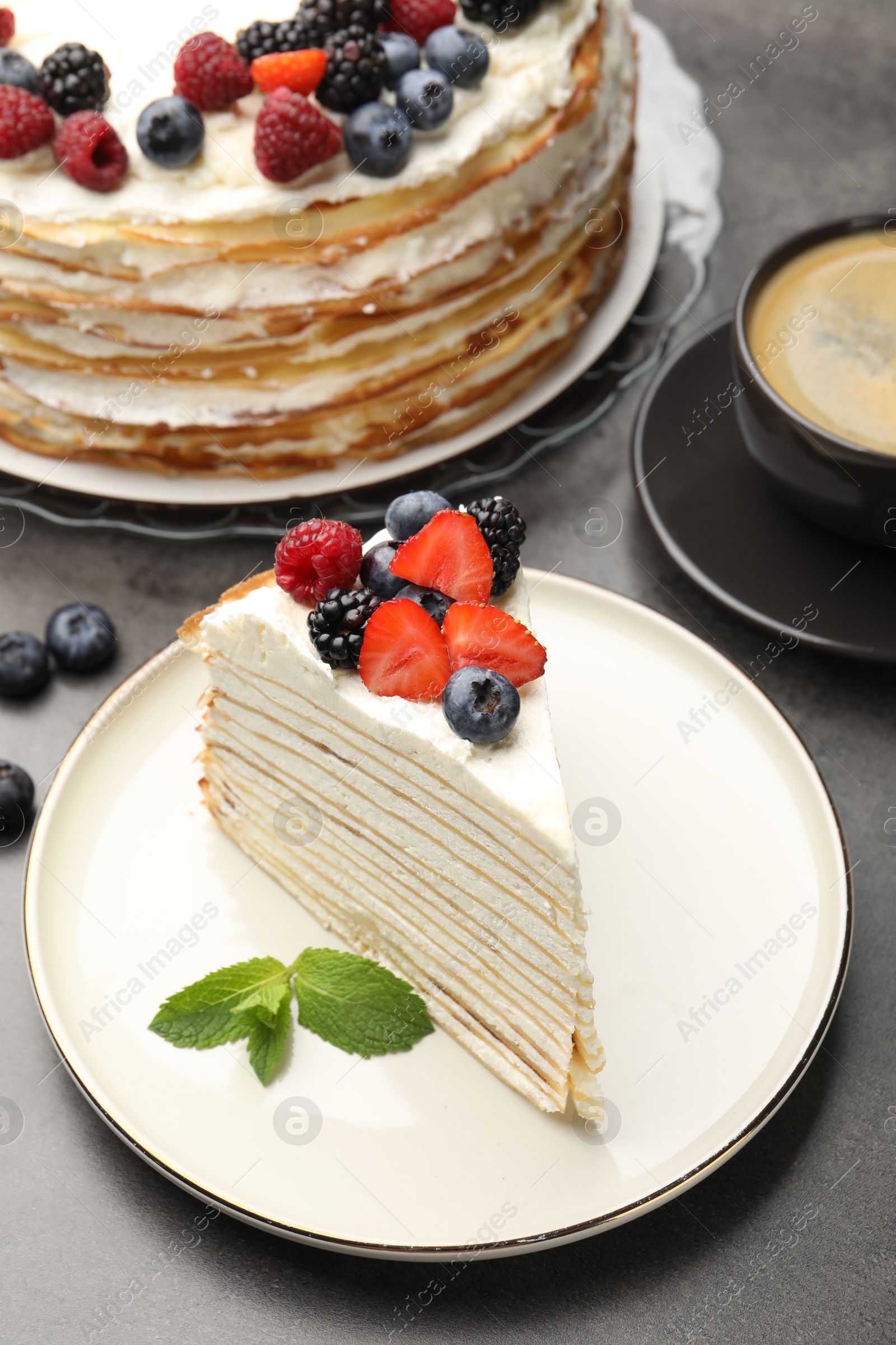 Photo of Piece of tasty crepe cake with berries served on grey table, closeup