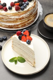 Photo of Piece of tasty crepe cake with berries served on grey table, closeup