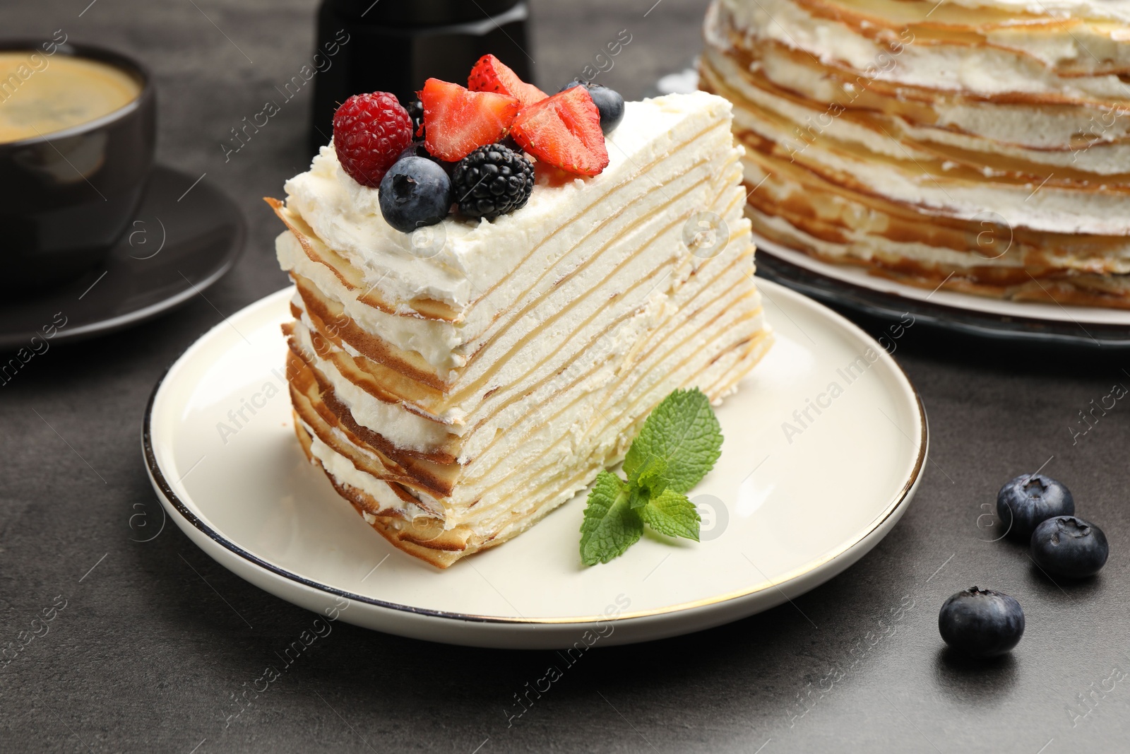Photo of Piece of tasty crepe cake with berries served on grey table, closeup