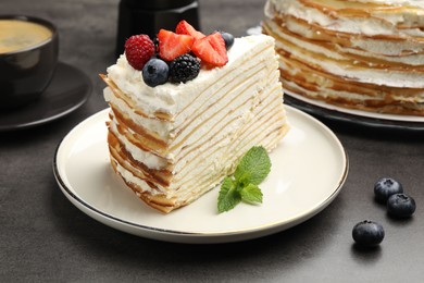 Photo of Piece of tasty crepe cake with berries served on grey table, closeup