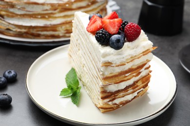 Photo of Piece of tasty crepe cake with berries on grey table, closeup