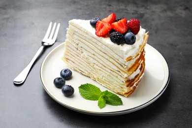 Photo of Piece of tasty crepe cake with berries served on grey table, closeup