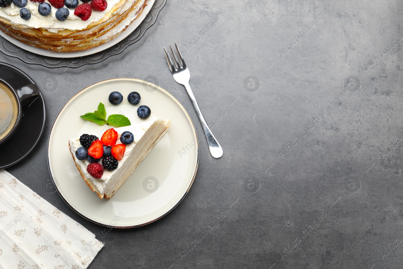 Photo of Piece of tasty crepe cake with berries served on grey table, flat lay. Space for text