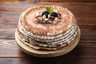 Photo of Delicious crepe cake with chocolate, nuts, blackberries and cocoa powder on wooden table, closeup