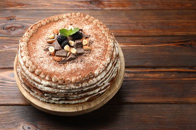 Photo of Delicious crepe cake with chocolate, nuts, blackberries and cocoa powder on wooden table, closeup. Space for text