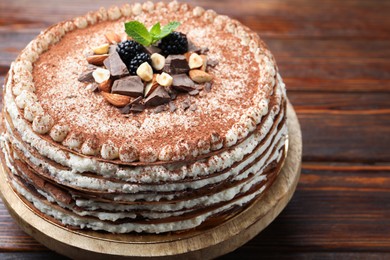 Photo of Delicious crepe cake with chocolate, nuts, blackberries and cocoa powder on wooden table, closeup