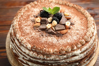 Photo of Delicious crepe cake with chocolate, nuts, blackberries and cocoa powder on wooden table, closeup