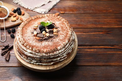 Photo of Delicious crepe cake with chocolate, nuts, blackberries and cocoa powder on wooden table. Space for text