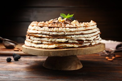 Photo of Delicious crepe cake with chocolate, nuts, blackberries and cocoa powder on wooden table, closeup