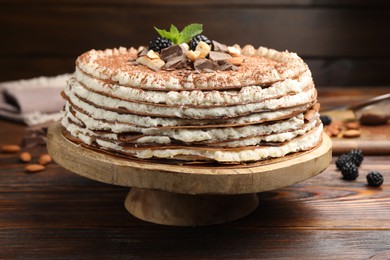 Photo of Delicious crepe cake with chocolate, nuts, blackberries and cocoa powder on wooden table, closeup