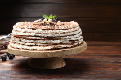 Photo of Delicious crepe cake with chocolate, nuts, blackberries and cocoa powder on wooden table, closeup