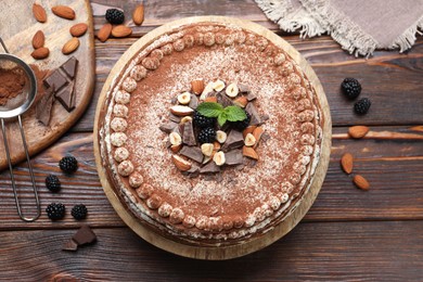 Photo of Delicious crepe cake with chocolate, nuts, blackberries and cocoa powder on wooden table, flat lay