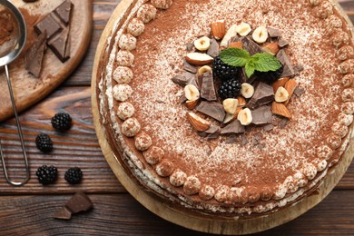 Photo of Delicious crepe cake with chocolate, nuts, blackberries and cocoa powder on wooden table, flat lay
