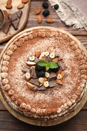 Photo of Delicious crepe cake with chocolate, nuts, blackberries and cocoa powder on wooden table, flat lay