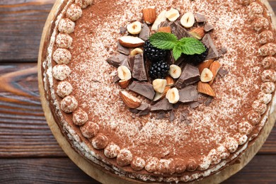 Photo of Delicious crepe cake with chocolate, nuts, blackberries and cocoa powder on wooden table, top view