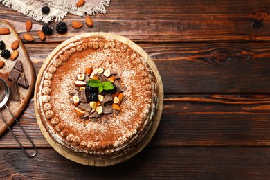Photo of Delicious crepe cake with chocolate, nuts, blackberries and cocoa powder on wooden table, flat lay. Space for text