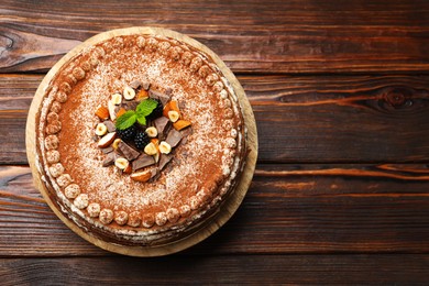 Photo of Delicious crepe cake with chocolate, nuts, blackberries and cocoa powder on wooden table, top view. Space for text