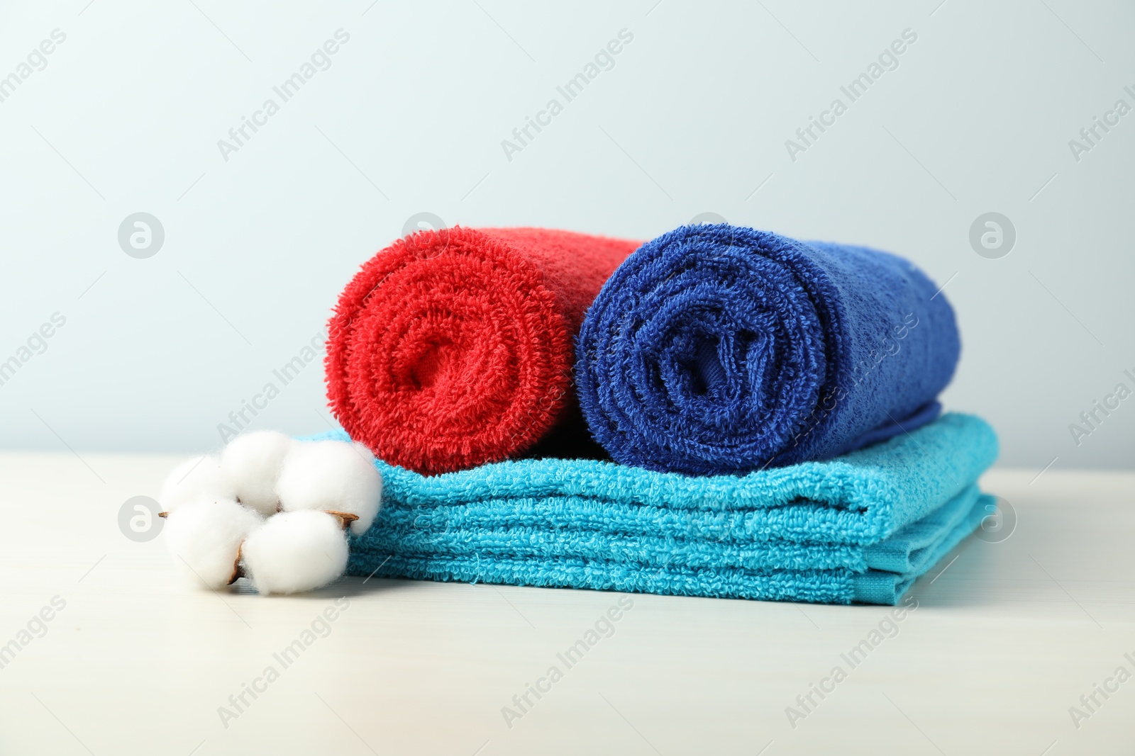 Photo of Colorful fresh terry towels and cotton flower on white table, closeup
