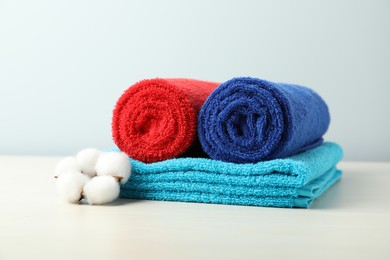Photo of Colorful fresh terry towels and cotton flower on white table, closeup